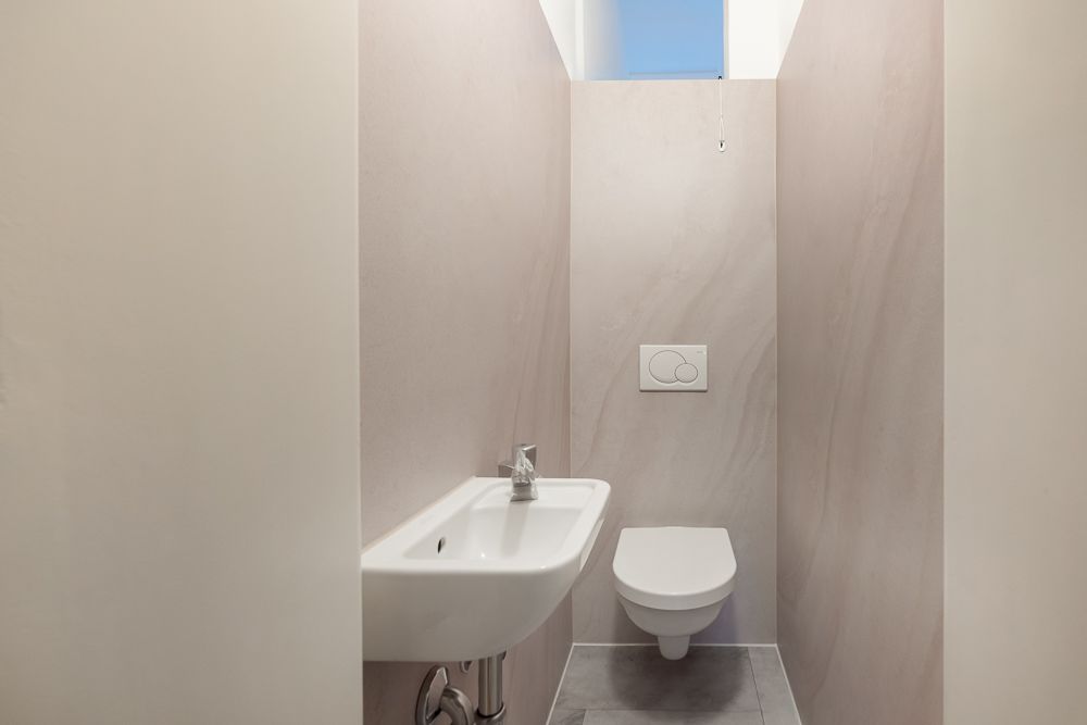 Kleines, modernes WC mit Wandtoilette, kleinem Waschbecken und Fenster oben.