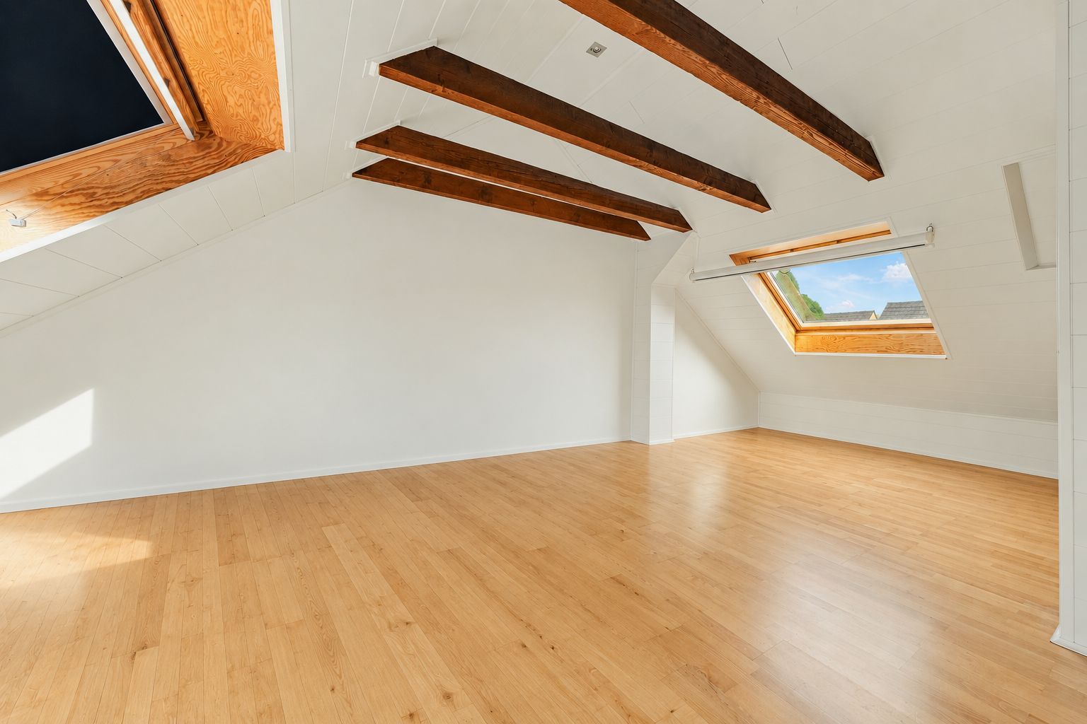 Großer leerer Dachbodenraum mit Holzboden, weißen Wänden und sichtbaren Holzbalken sowie Dachfenstern.