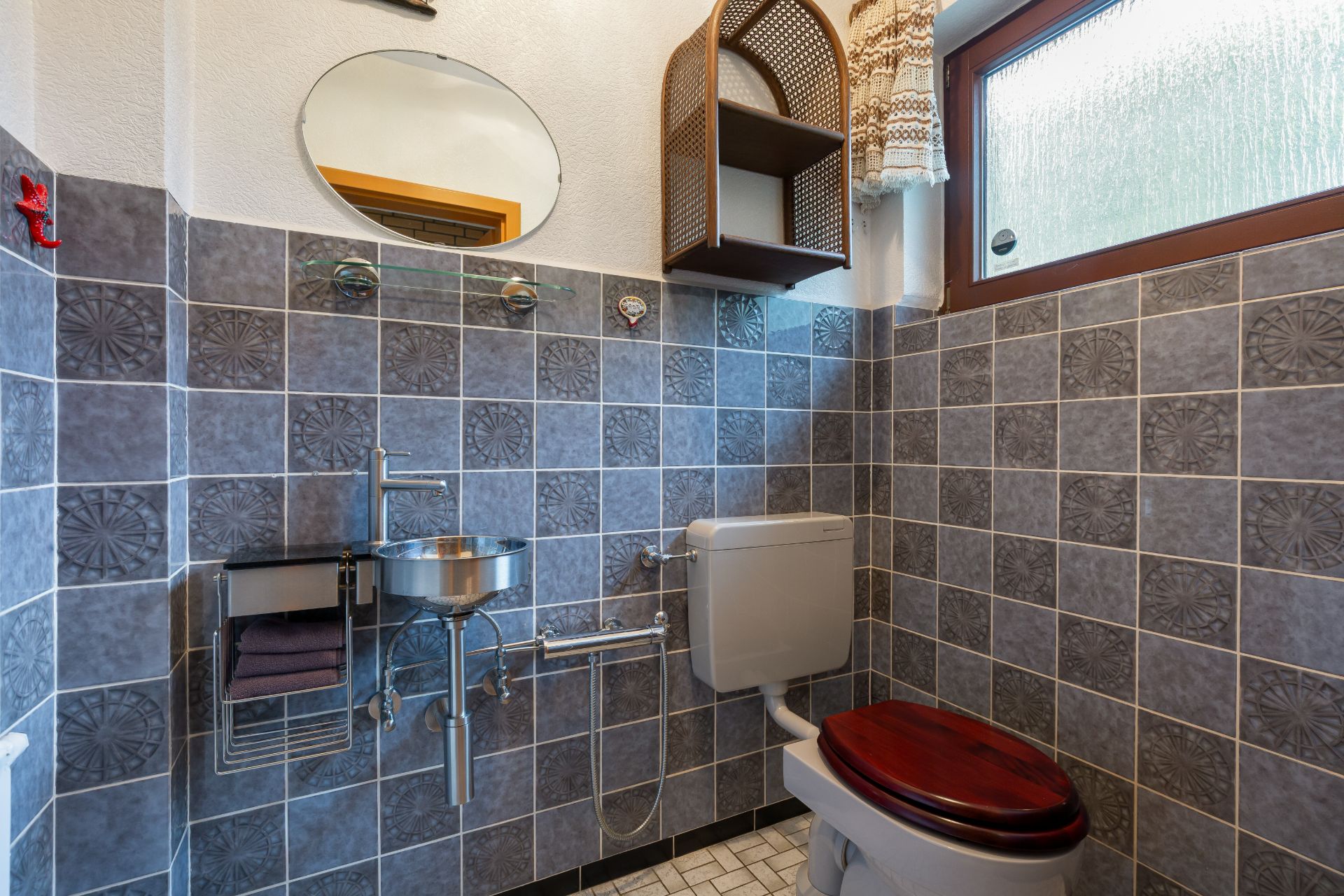 Kleines Badezimmer mit Toilette, rundem Waschbecken, Spiegel und Fenster mit Vorhang.