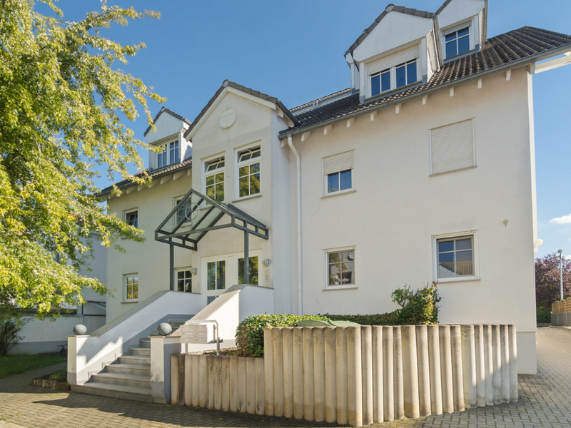 Modernes weißes Wohngebäude mit mehreren Fenstern, Vordach und Treppe zum Eingang.