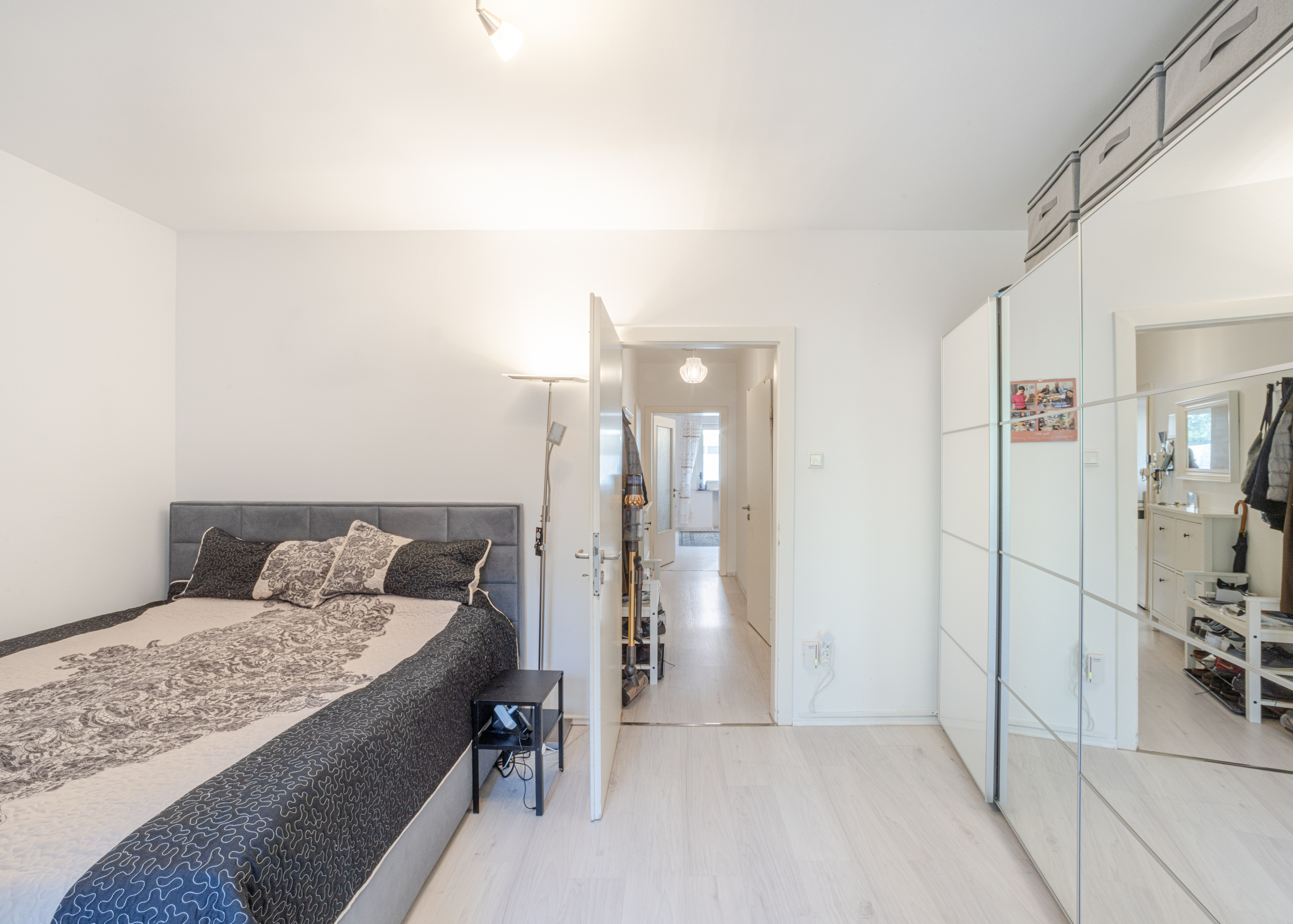 Helles Schlafzimmer mit Doppelbett, Nachttisch, Stehlampe und großem Spiegelschrank.