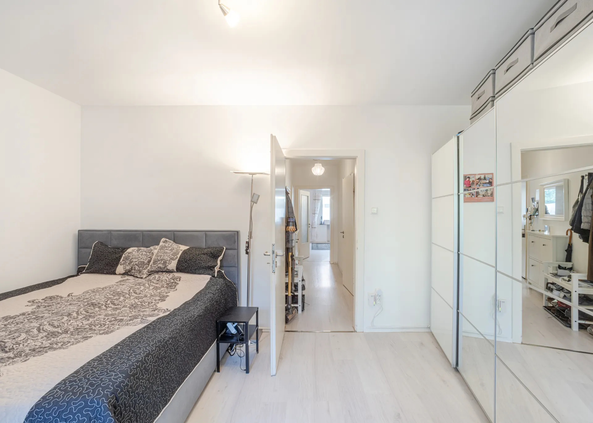 Helles Schlafzimmer mit Doppelbett, Nachttisch, Stehlampe und großem Spiegelschrank.