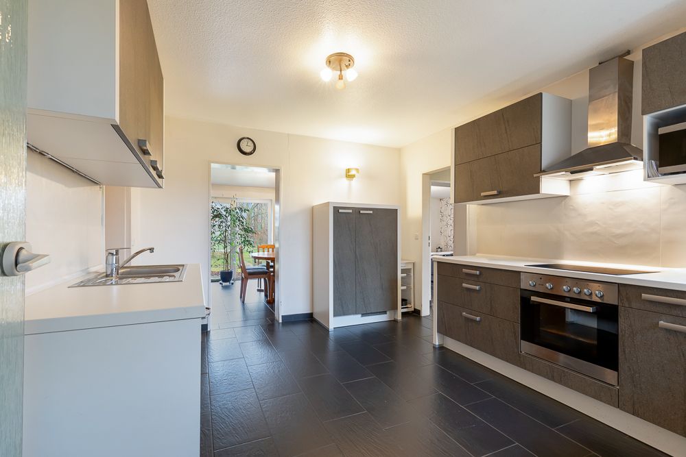 Moderne Küche mit dunklem Boden, Einbauherd, Spüle und Blick in ein Esszimmer.