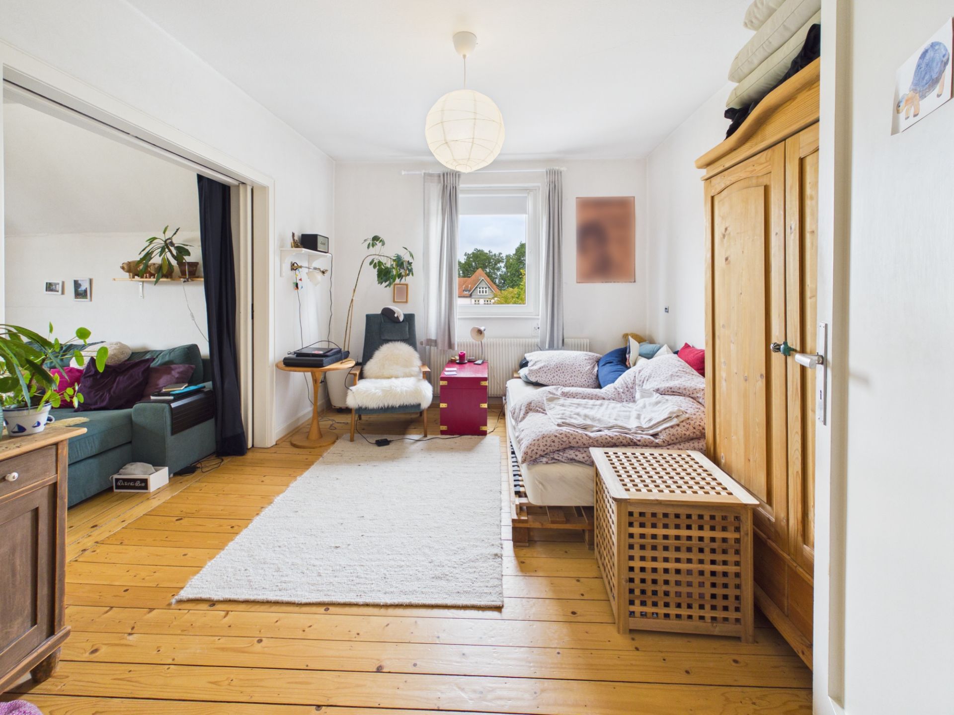 Helles Schlafzimmer mit Holzboden, Bett, Kleiderschrank und Fenster mit Blick nach draußen.