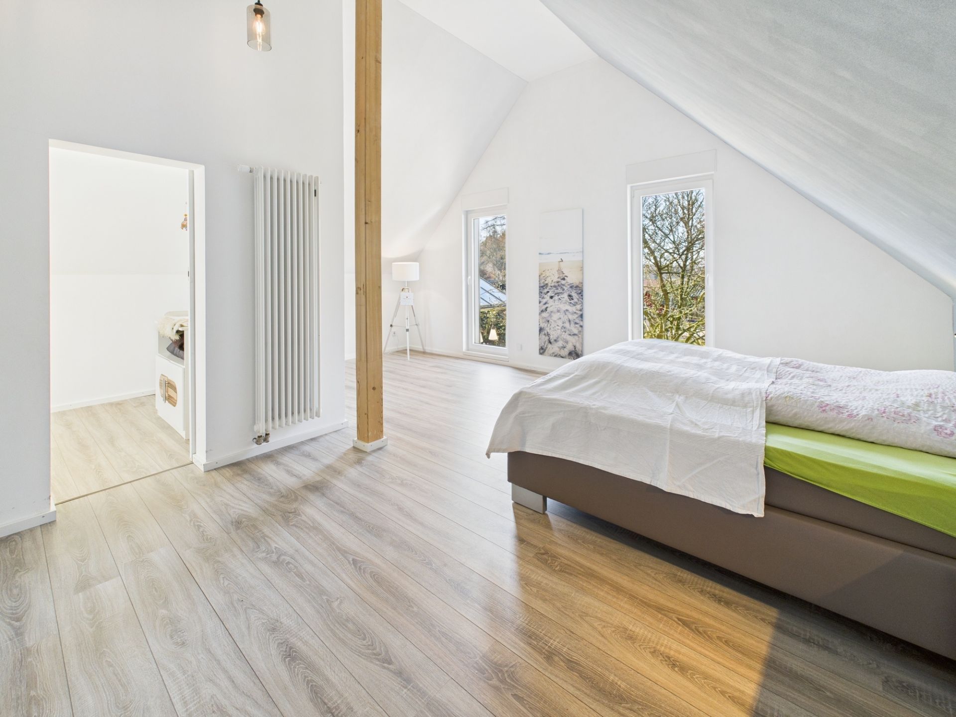 Helles Schlafzimmer mit großem Fenster, Holzboden, Bett und Stehlampe.