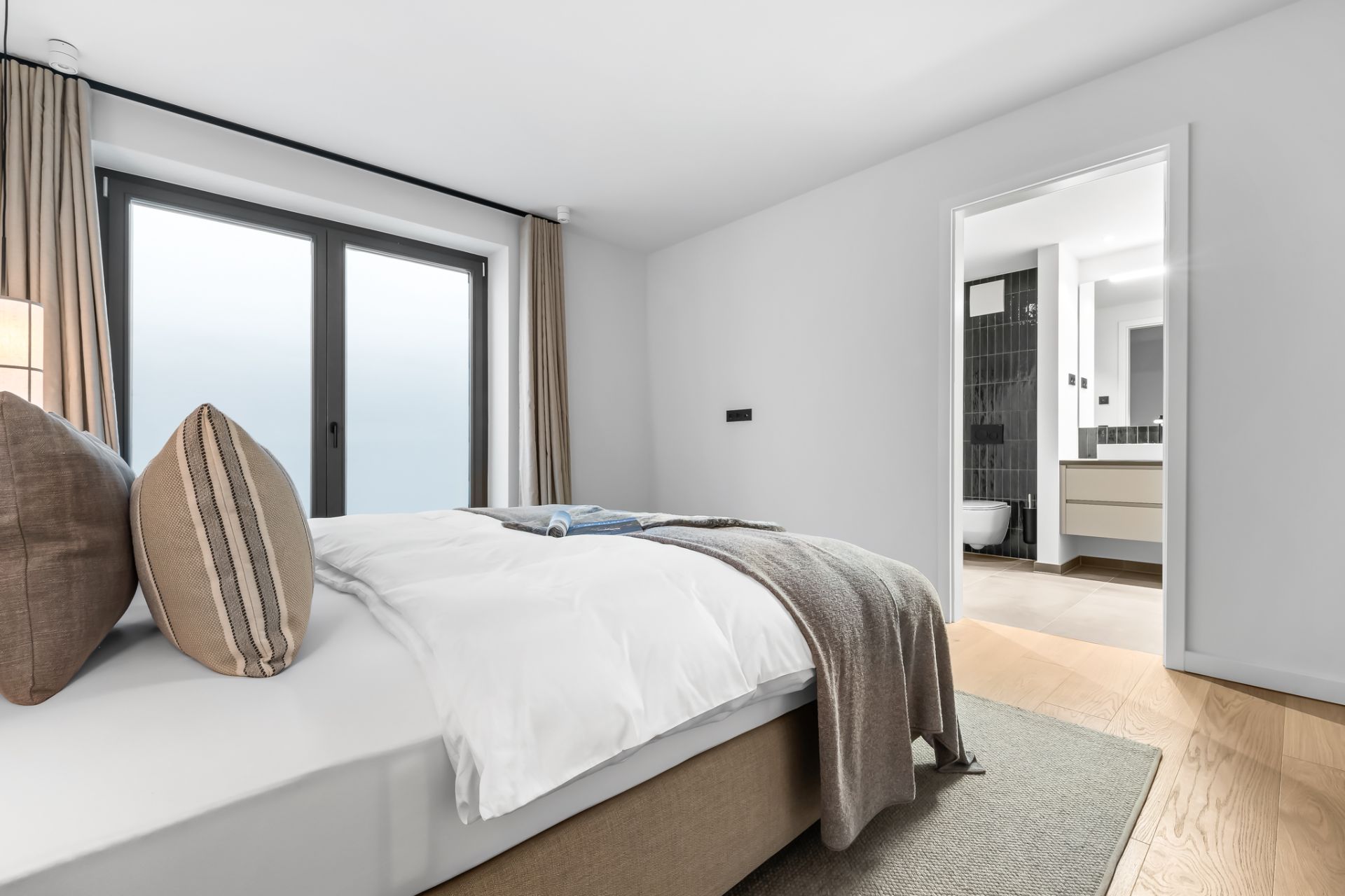 Modernes Schlafzimmer mit Doppelbett, großen Fenstern und Blick ins angrenzende Badezimmer.