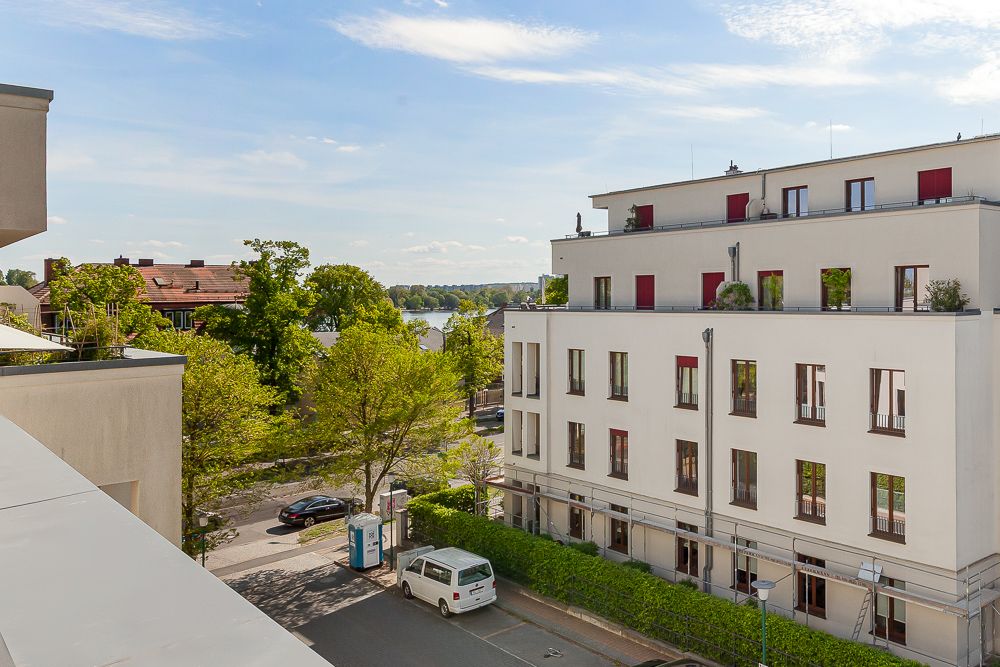 Blick auf ein modernes Wohngebäude mit mehreren Etagen und einige Bäume am Straßenrand.