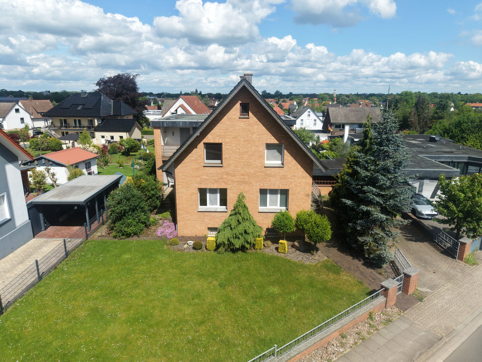 Zweistöckiges Haus mit Satteldach und großem Vorgarten, umgeben von weiteren Wohnhäusern.