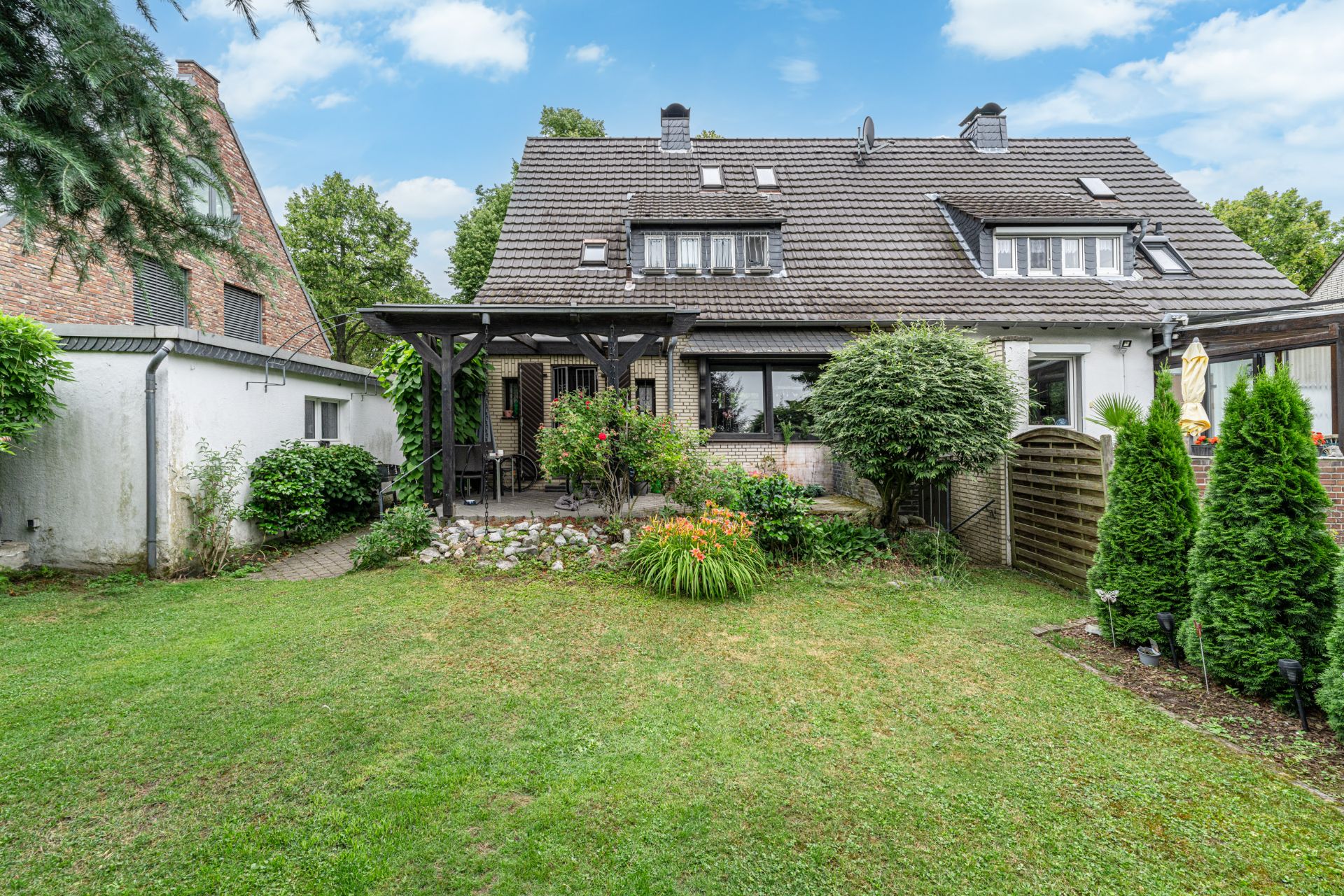 Garten mit Rasen, Terrasse mit Pergola und Pflanzen hinter einem Einfamilienhaus.
