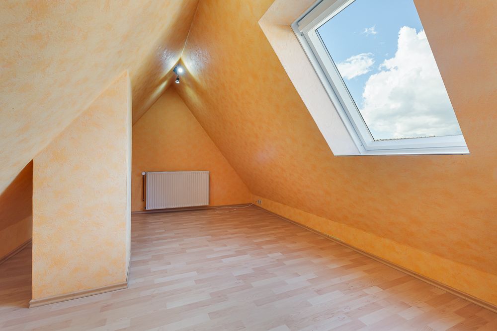 Dachzimmer mit gelben Wänden, großem Dachfenster und hellem Holzboden.