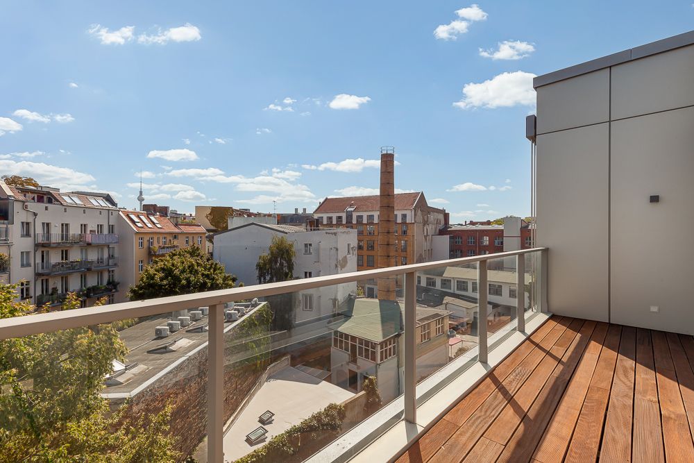 Balkon mit Holzfußboden und Glasgeländer, Blick auf städtische Gebäude bei Sonnenschein.