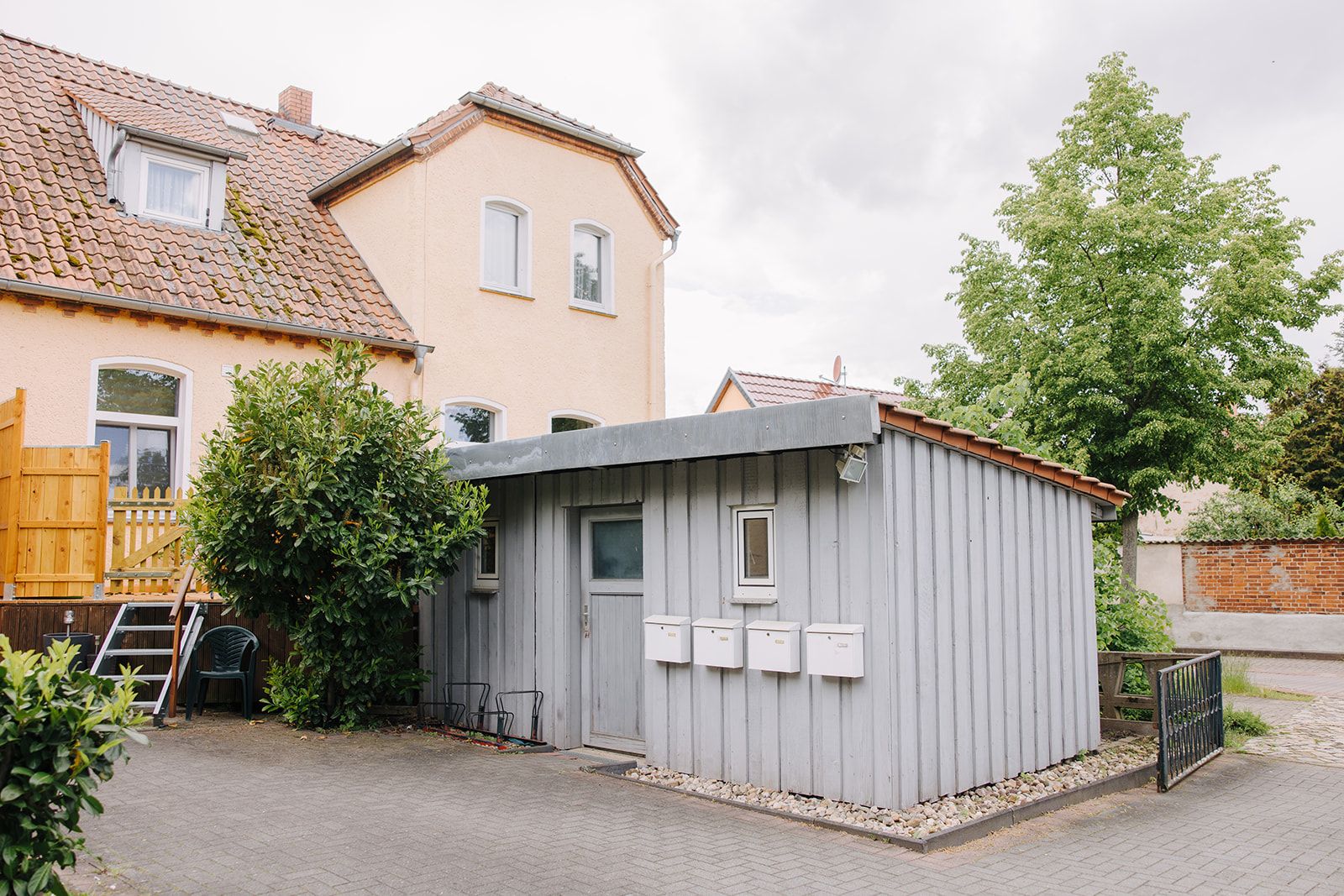 Gelbes Wohnhaus mit grauem Nebengebäude und mehreren Briefkästen davor.