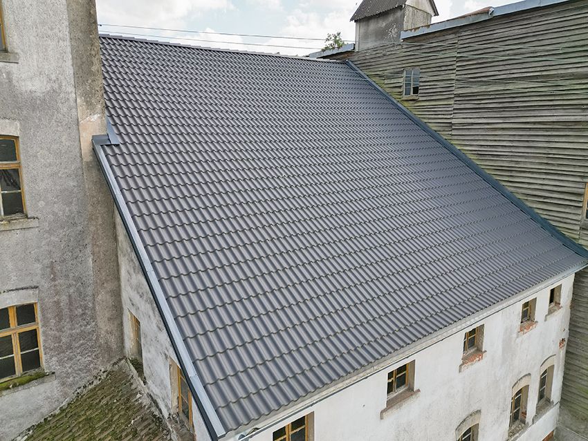 Großes Wohnhaus mit einem neuen grauen Dach aus Metallziegeln, mehrere Fenster sind sichtbar.