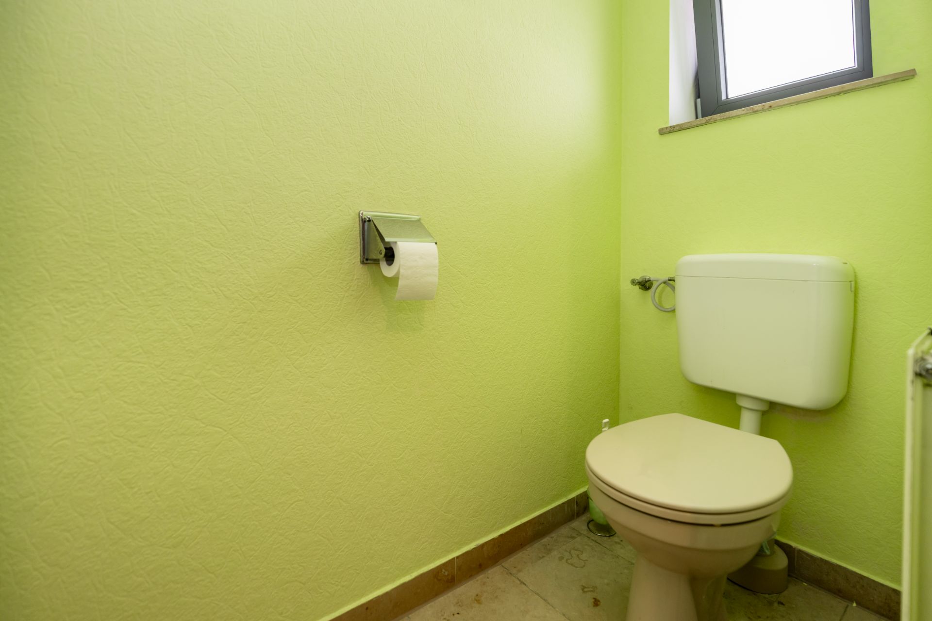 Kleines Badezimmer mit WC, grün gestrichenen Wänden und Fenster.