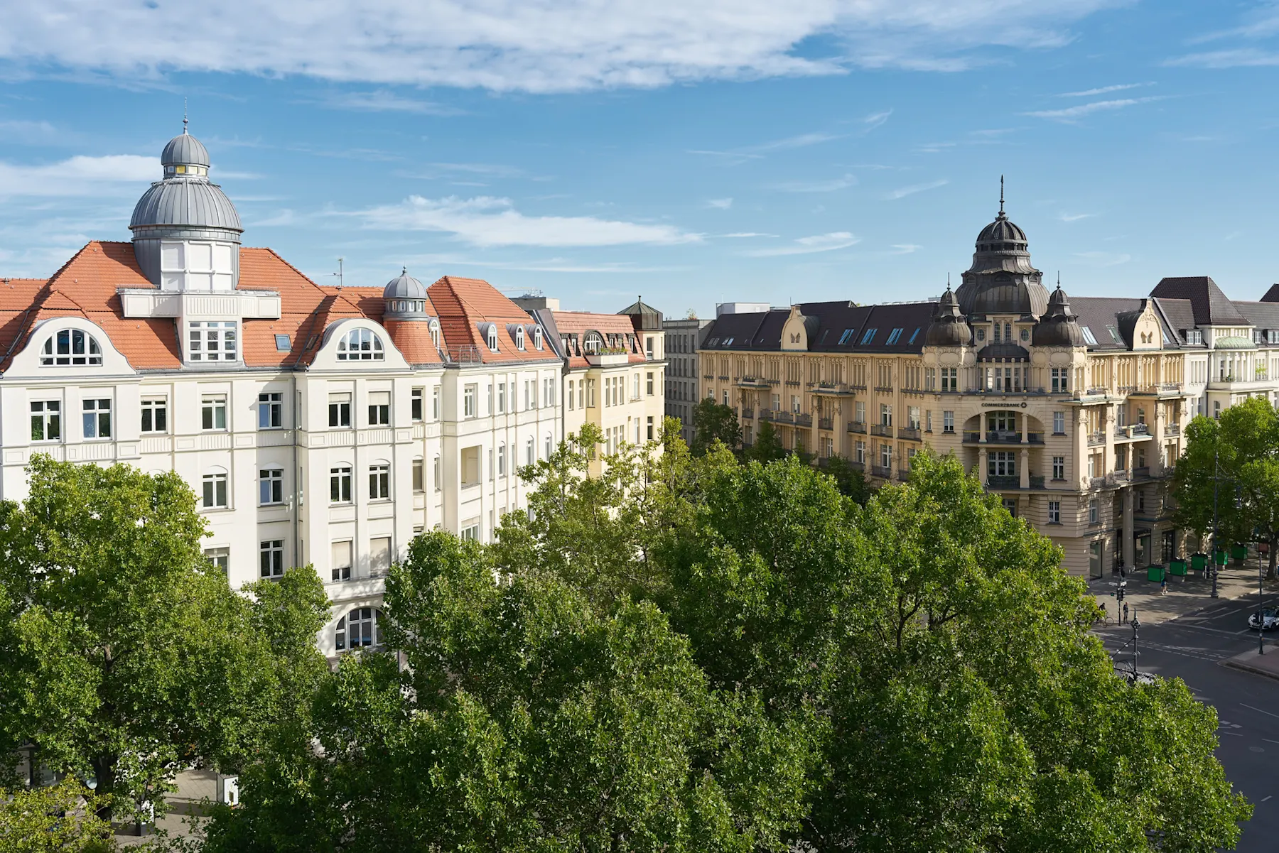 Blick auf historische Wohngebäude mit Türmen und Bäumen im Vordergrund bei blauem Himmel.