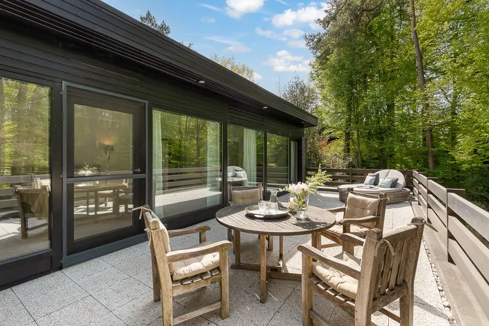 Große Terrasse mit Holztisch, vier Stühlen und Sitzbereich, umgeben von Bäumen.