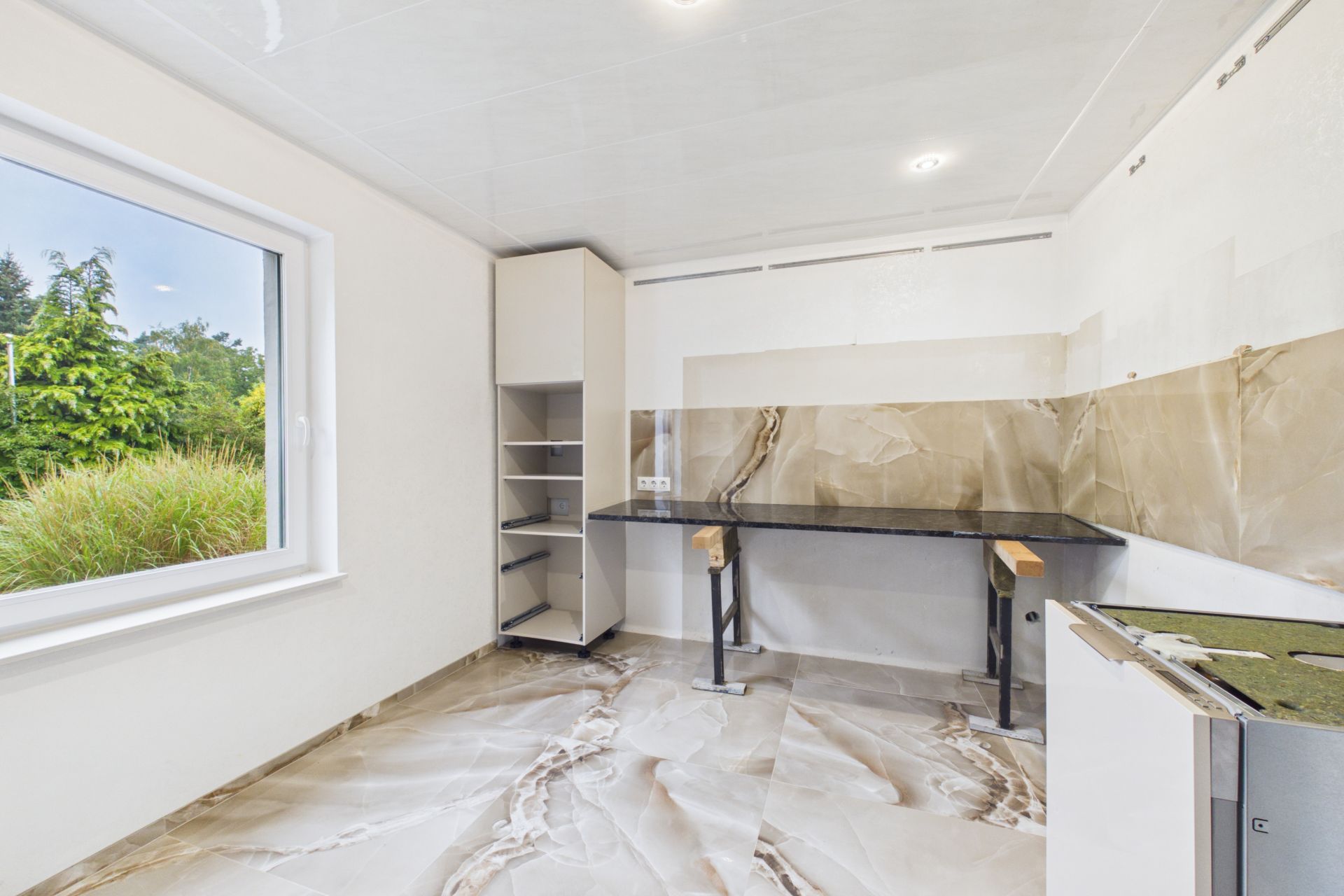 Leere moderne Küche mit Marmorfliesen, großem Fenster und Arbeitsplattenmontage.