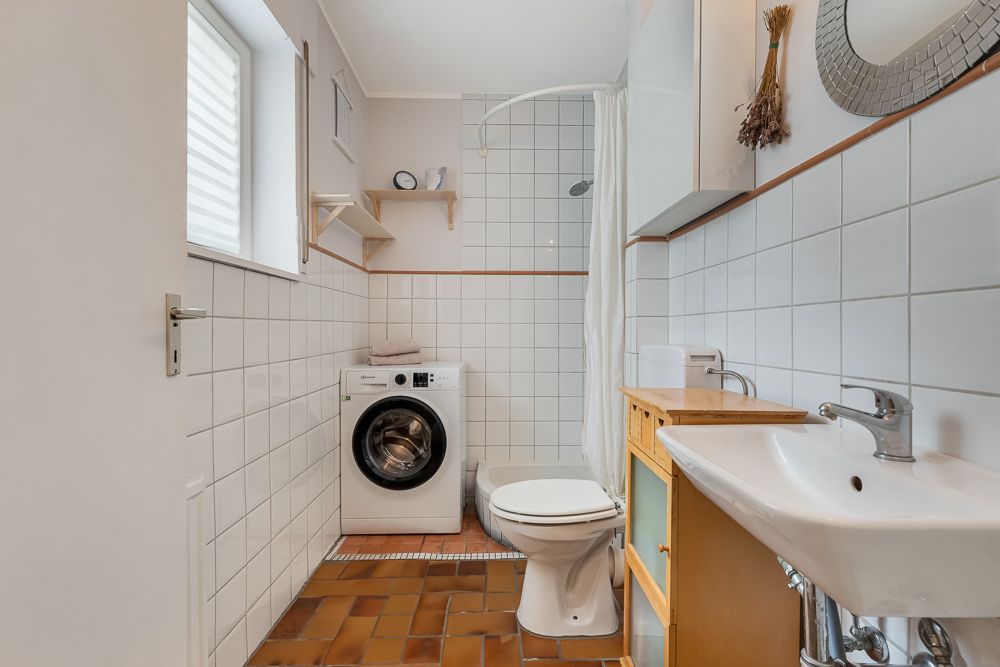 Badezimmer mit Waschmaschine, Toilette, Waschbecken und Dusche mit weiß gefliesten Wänden.