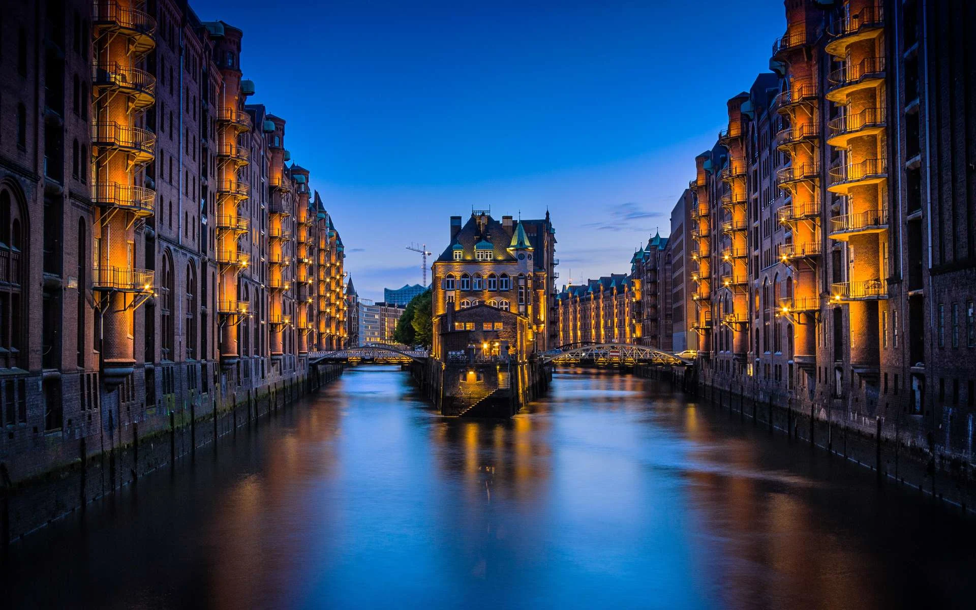 Beleuchtete Backsteingebäude an einem Kanal bei Dämmerung, Gebäude in der Mitte mit Brücken.