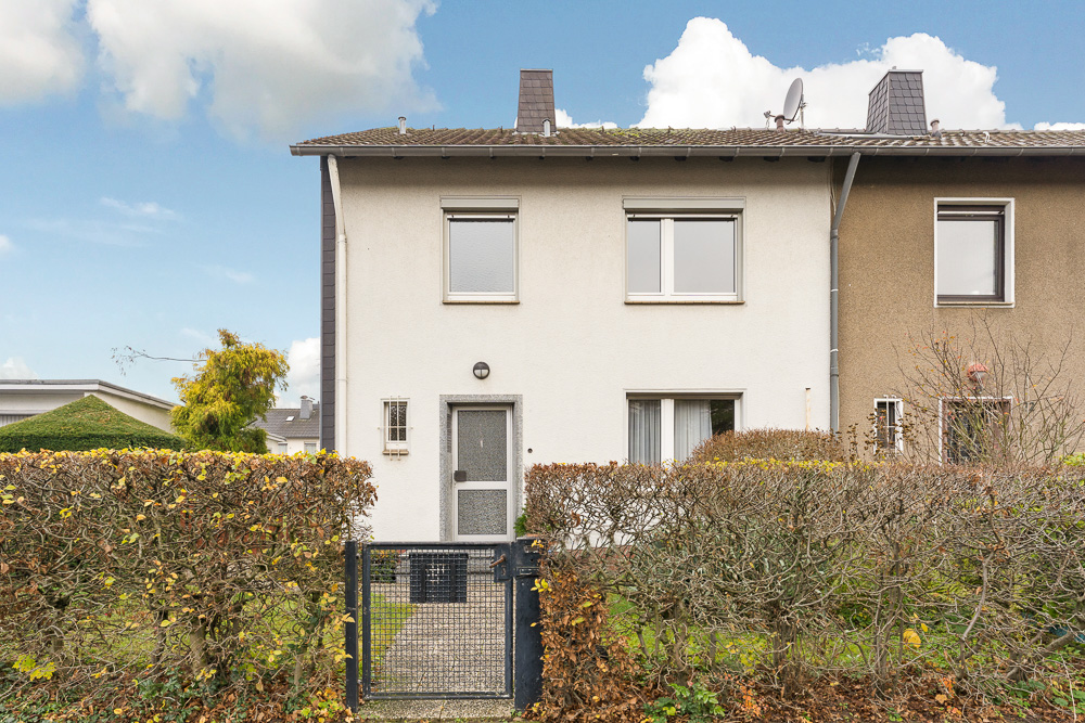 Zweistöckiges Wohnhaus mit weißer Fassade und Vorgarten, Hecke und Gartentor im Vordergrund.