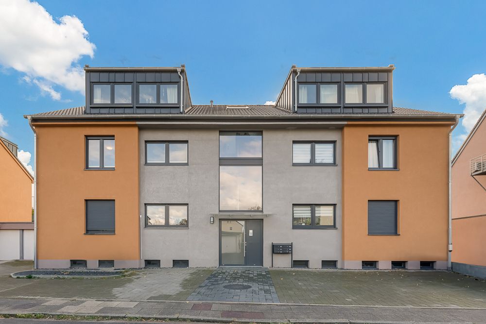 Modernes Mehrfamilienhaus mit orange-grauer Fassade und großen Fenstern, Vorderansicht.