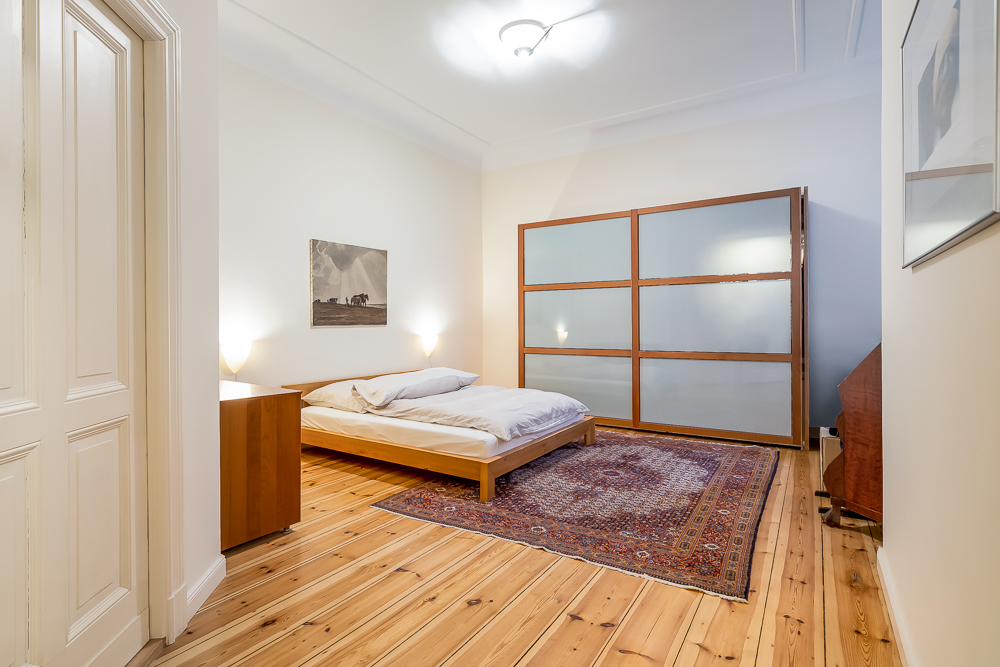 Helles Schlafzimmer mit Holzboden, Bett, Nachttisch, großem Teppich und Schiebetürenschrank.