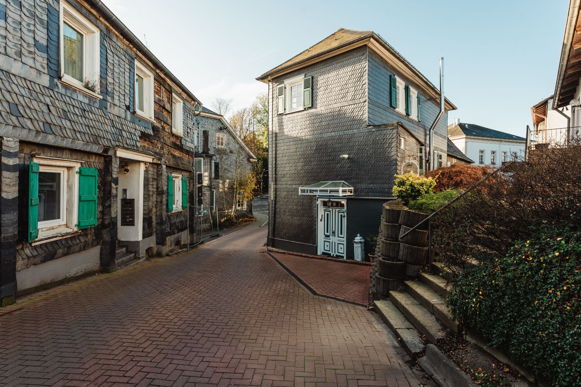 Gepflasterte Straße mit alten Wohnhäusern, Fassaden aus Schiefer und grünen Fensterläden.