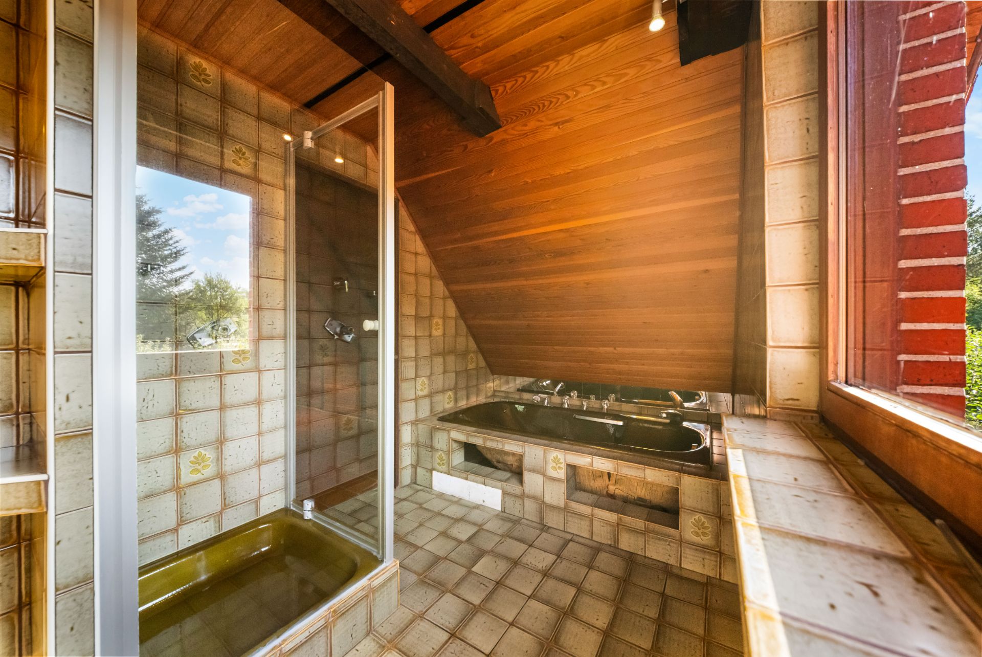 Badezimmer mit gelber Dusche, brauner Badewanne und gefliestem Boden, Holzdecke, großes Fenster.