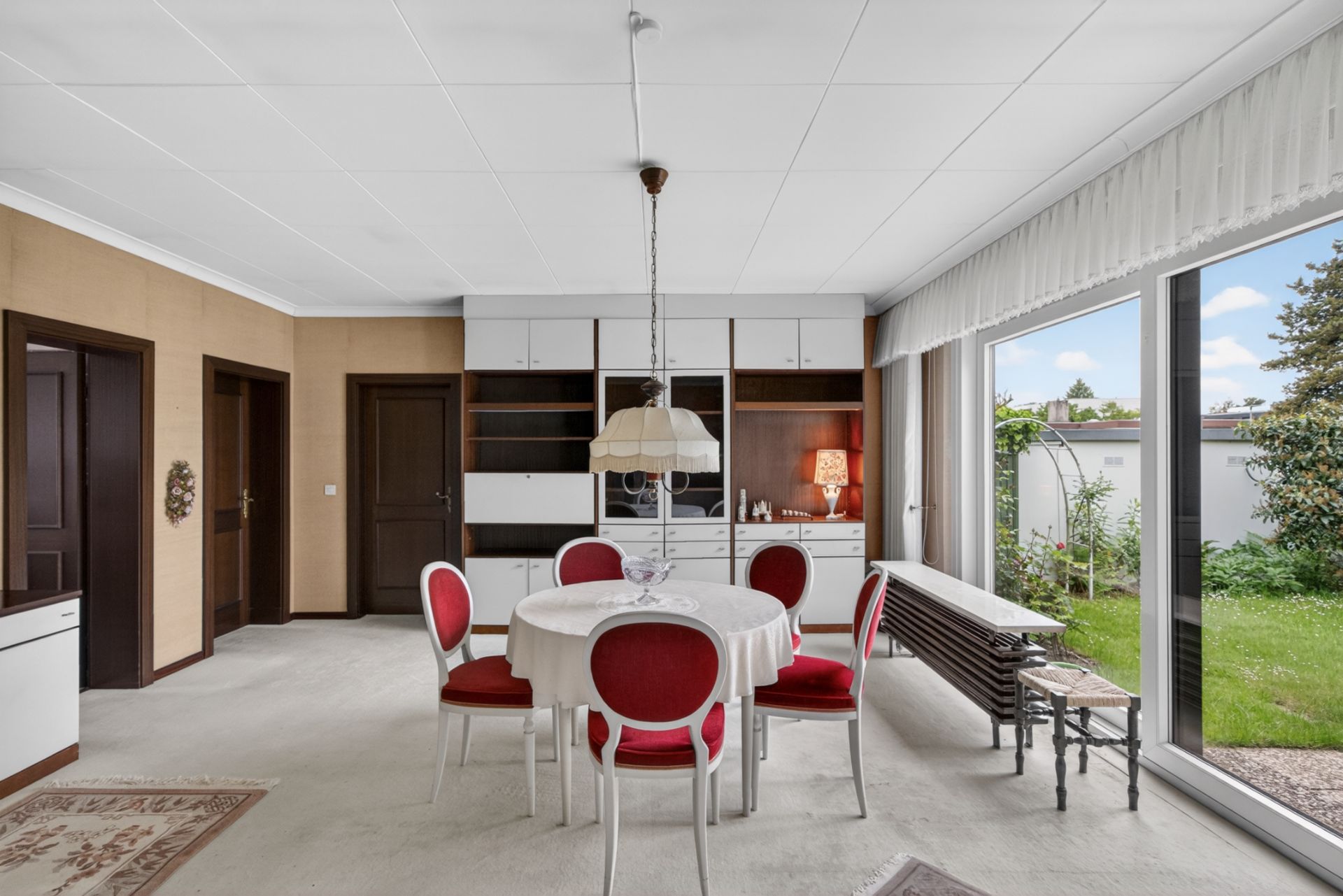 Esszimmer mit rundem Tisch, vier roten Stühlen und großen Fenstern mit Blick in den Garten.