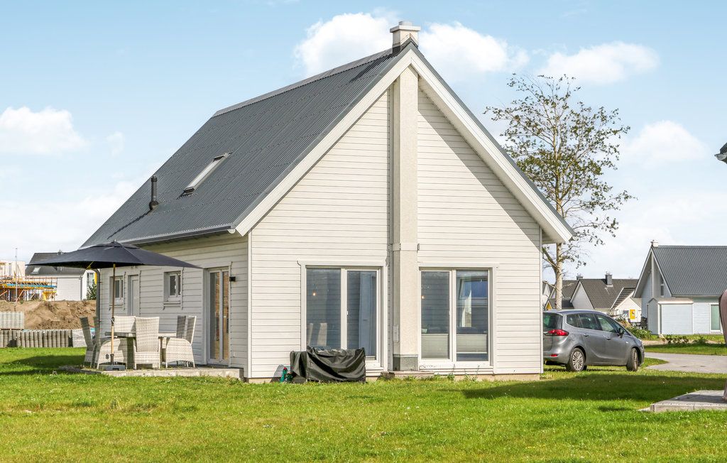 Modernes, helles Einfamilienhaus mit Terrasse, Gartenmöbeln und Auto auf grüner Wiese.