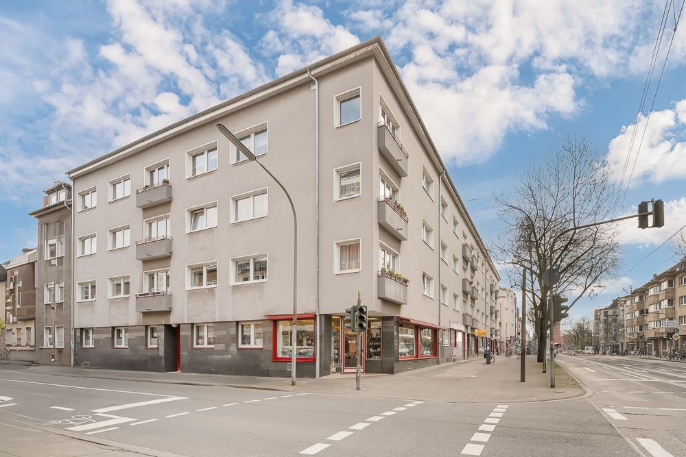 Mehrstöckiges Wohnhaus an einer Straßenecke mit Balkonen und Geschäften im Erdgeschoss.