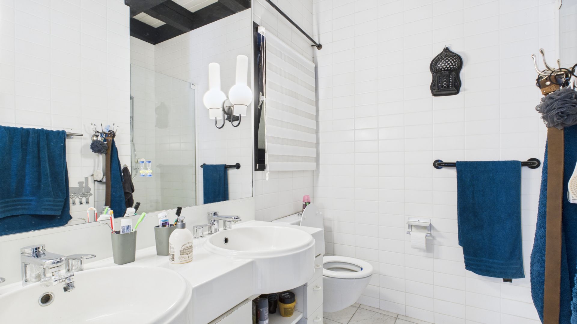 Helles Badezimmer mit zwei Waschbecken, großem Spiegel, WC und blauen Handtüchern.