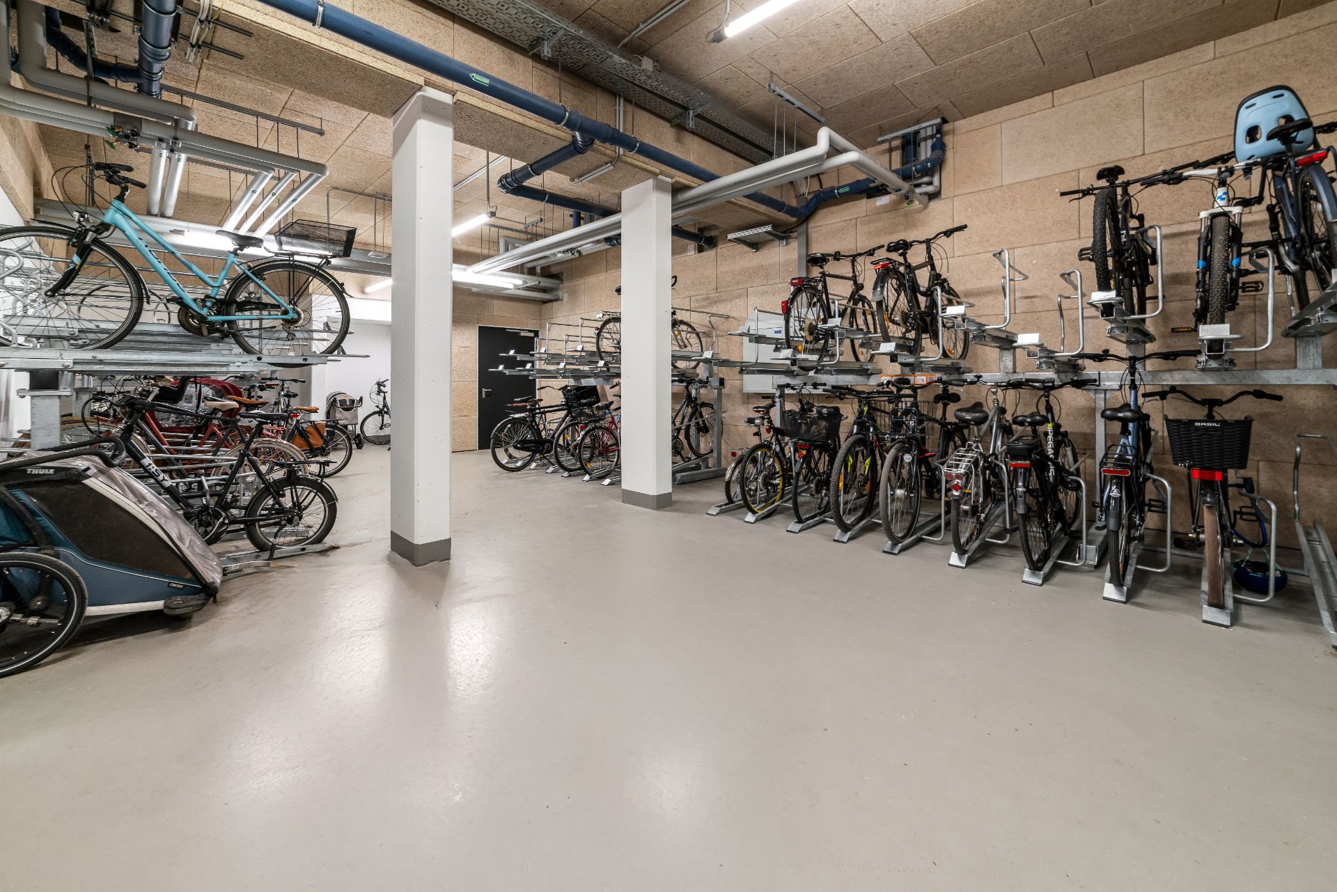 Fahrradraum mit mehreren abgestellten Fahrrädern auf Fahrradständern an den Wänden.