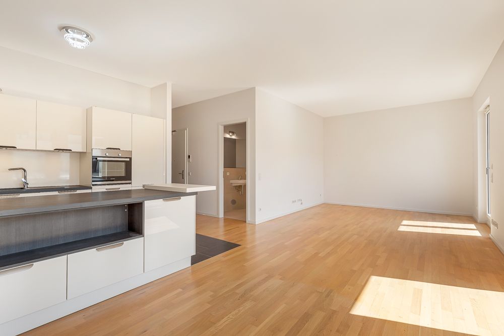 Helle Wohnung mit offener Einbauküche, Holzfußboden und Zugang zum Badezimmer.