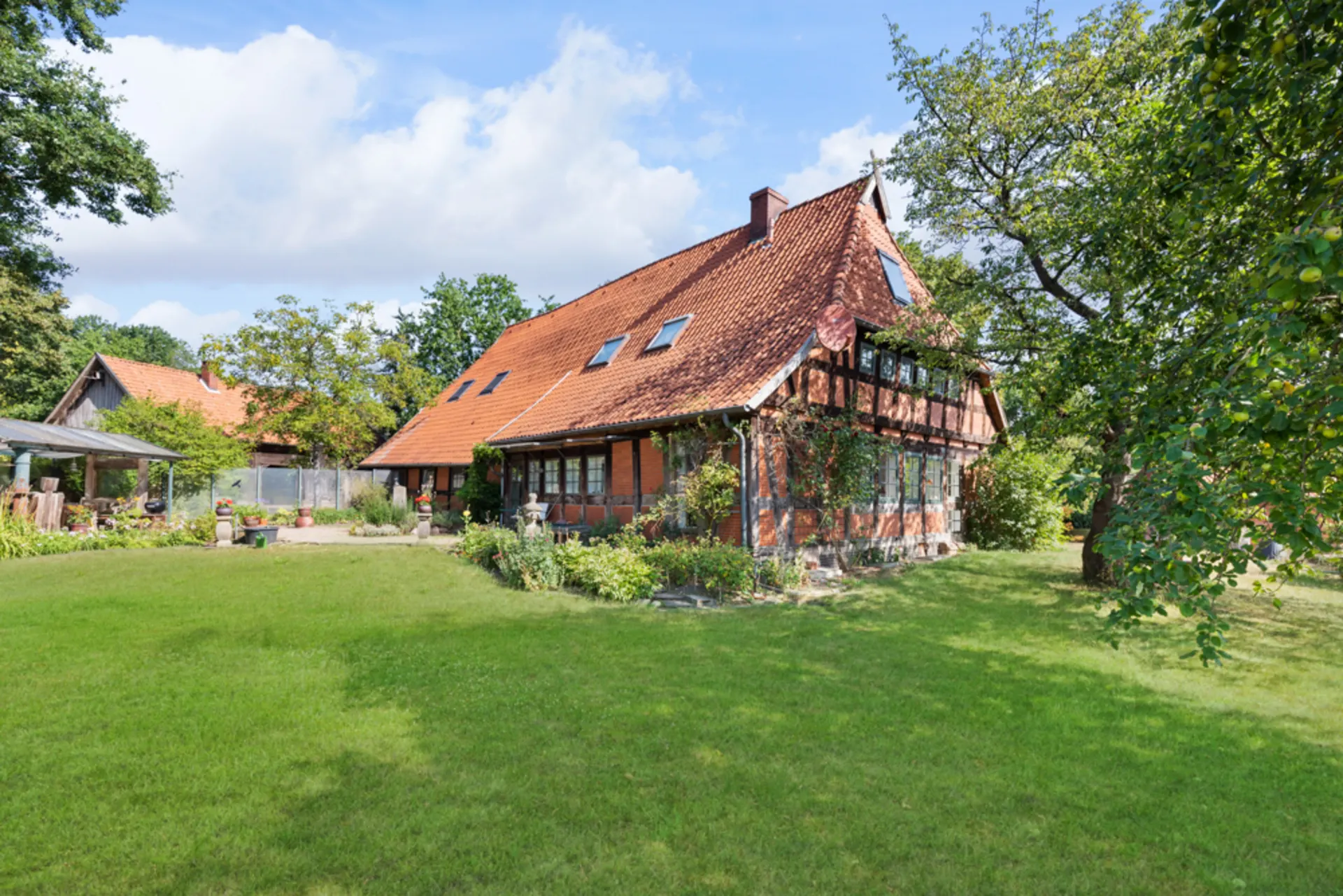 Großes Fachwerkhaus mit rotem Dach und Garten, Bäume und Wiese im Vordergrund.