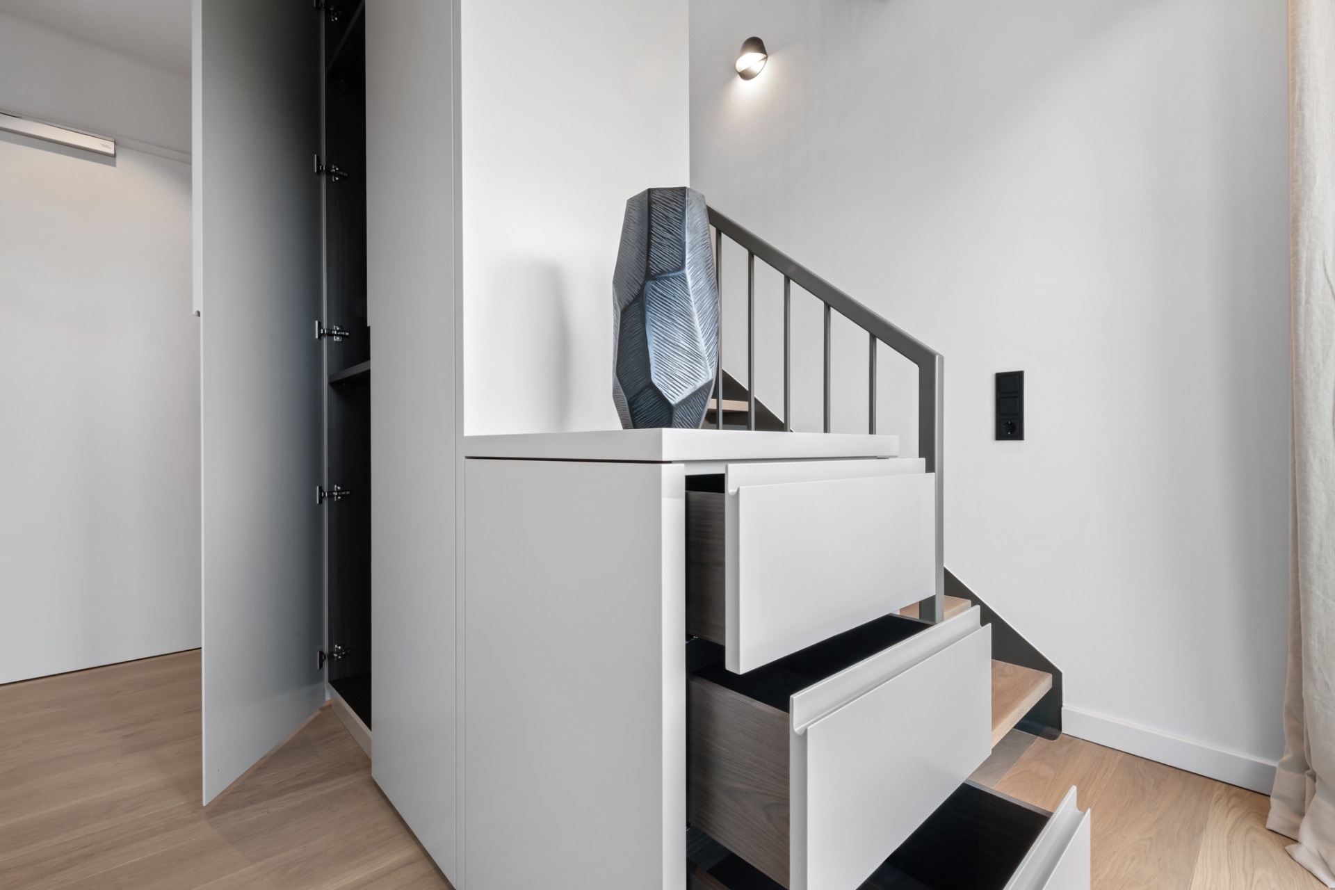 Moderne Treppe mit weißen Schubladen und geöffneter Tür zu einem Einbauschrank.