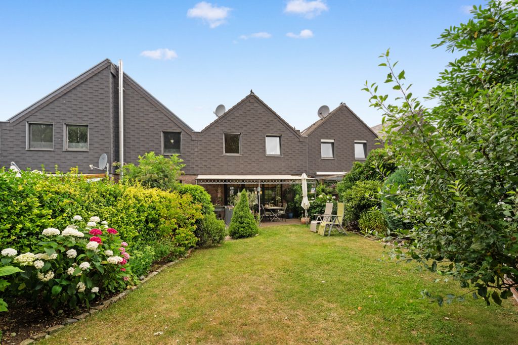 Rückansicht eines Reihenhauses mit Garten, Terrassenmöbeln und grünen Pflanzen im Vordergrund.
