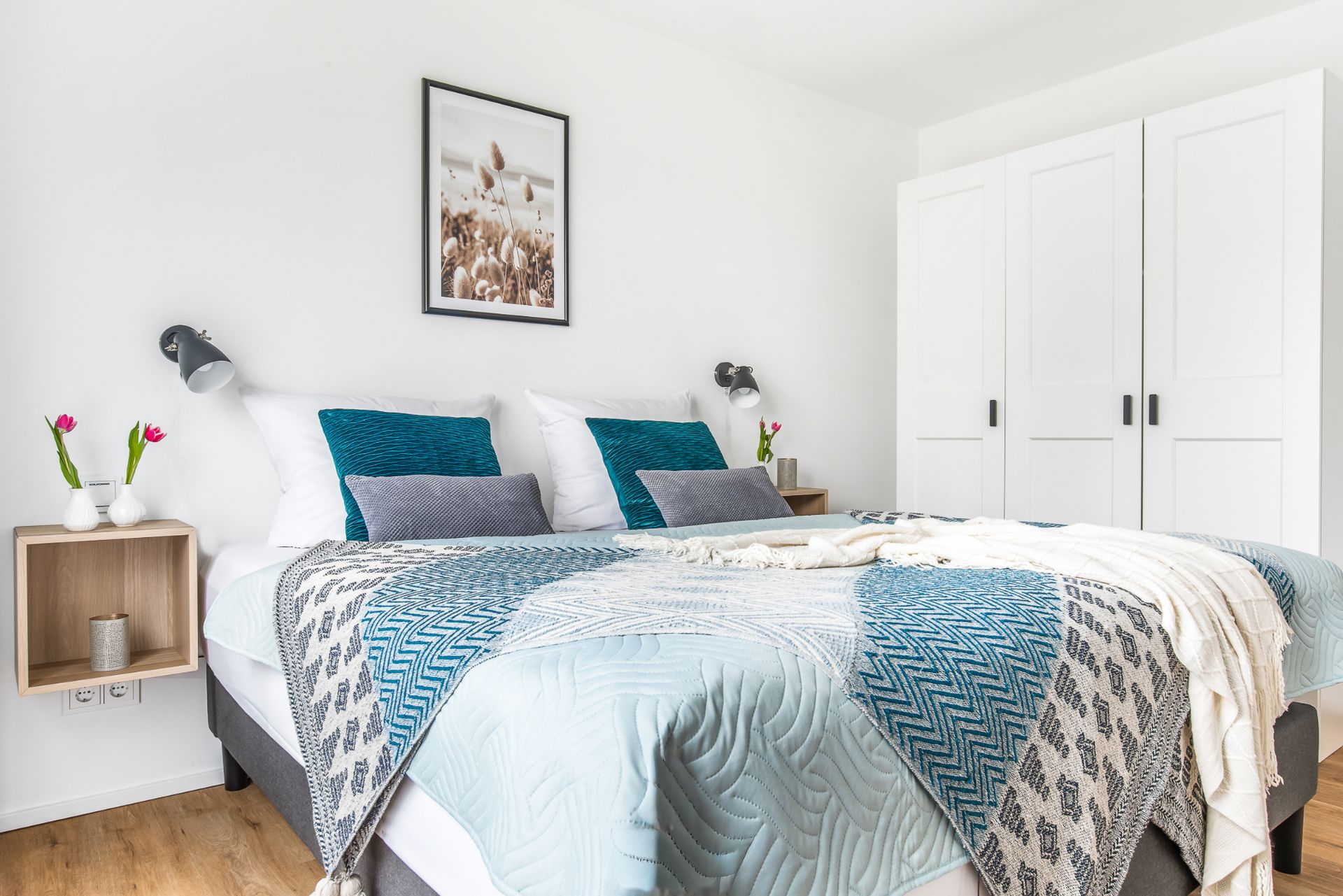 Helles Schlafzimmer mit Doppelbett, grauen und blauen Kissen, zwei Nachttischen und weißem Kleiderschrank.