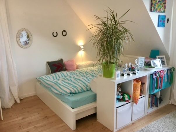 Helles Schlafzimmer mit Bett, Regal, Pflanzen und Dekoration in einer Dachgeschosswohnung.