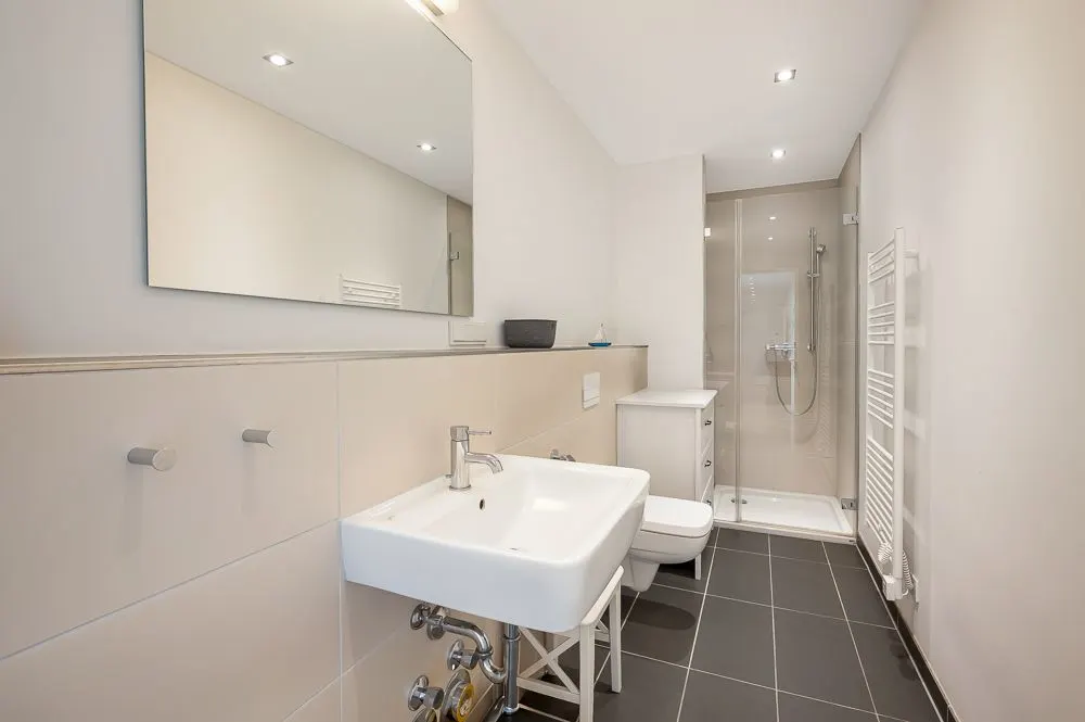 Modernes Badezimmer mit Waschbecken, Spiegel, Toilette, Dusche und Handtuchheizkörper.