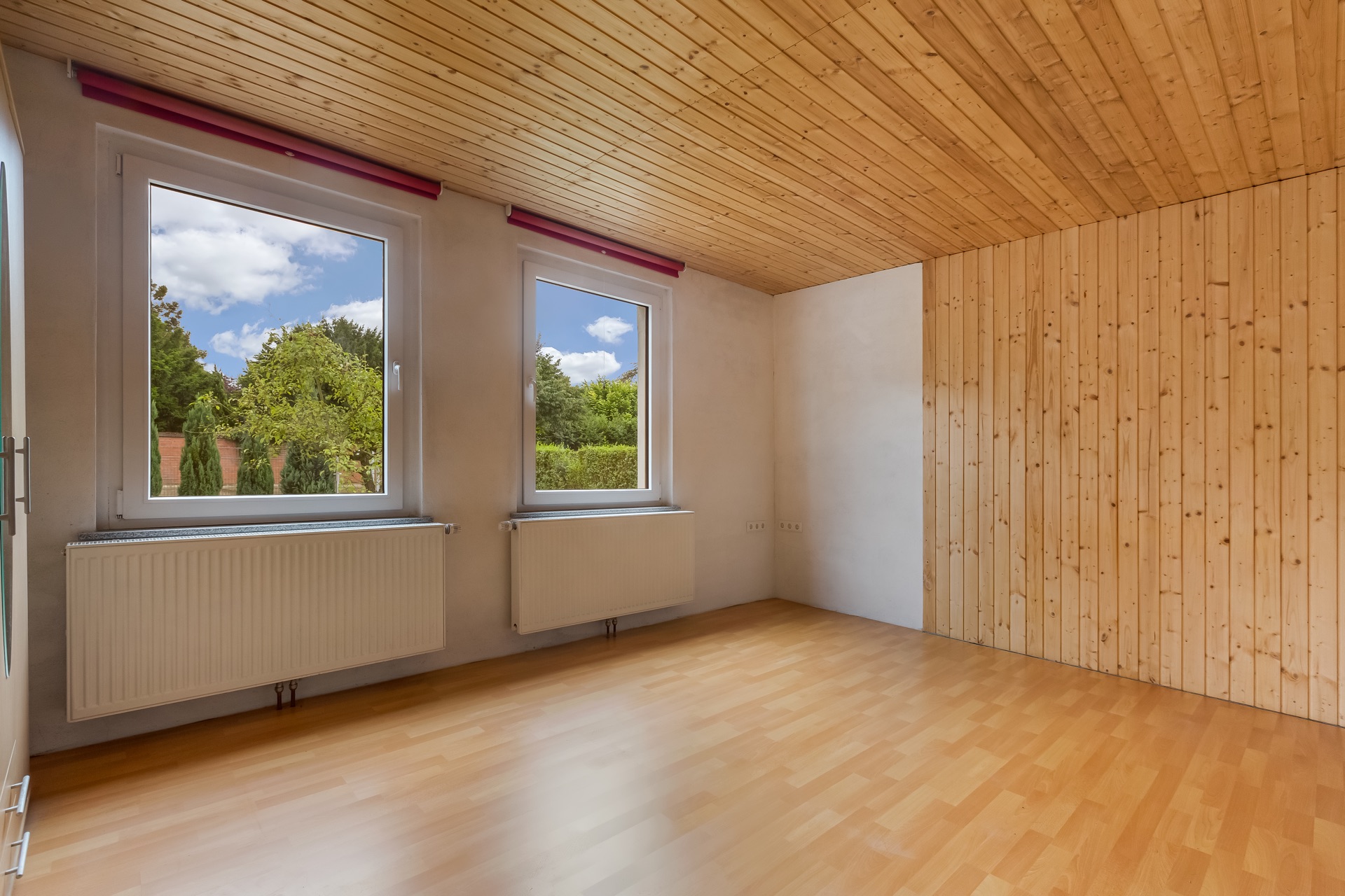 Leerer Raum mit Holzdecke, Holzfußboden, zwei Fenstern und holzverkleideter Wand.