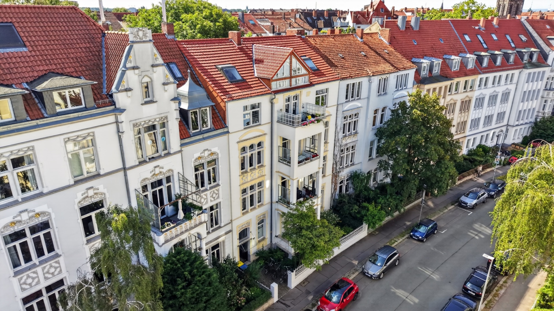Reihe von mehrstöckigen Wohnhäusern mit roten Dächern an einer baumbestandenen Straße.