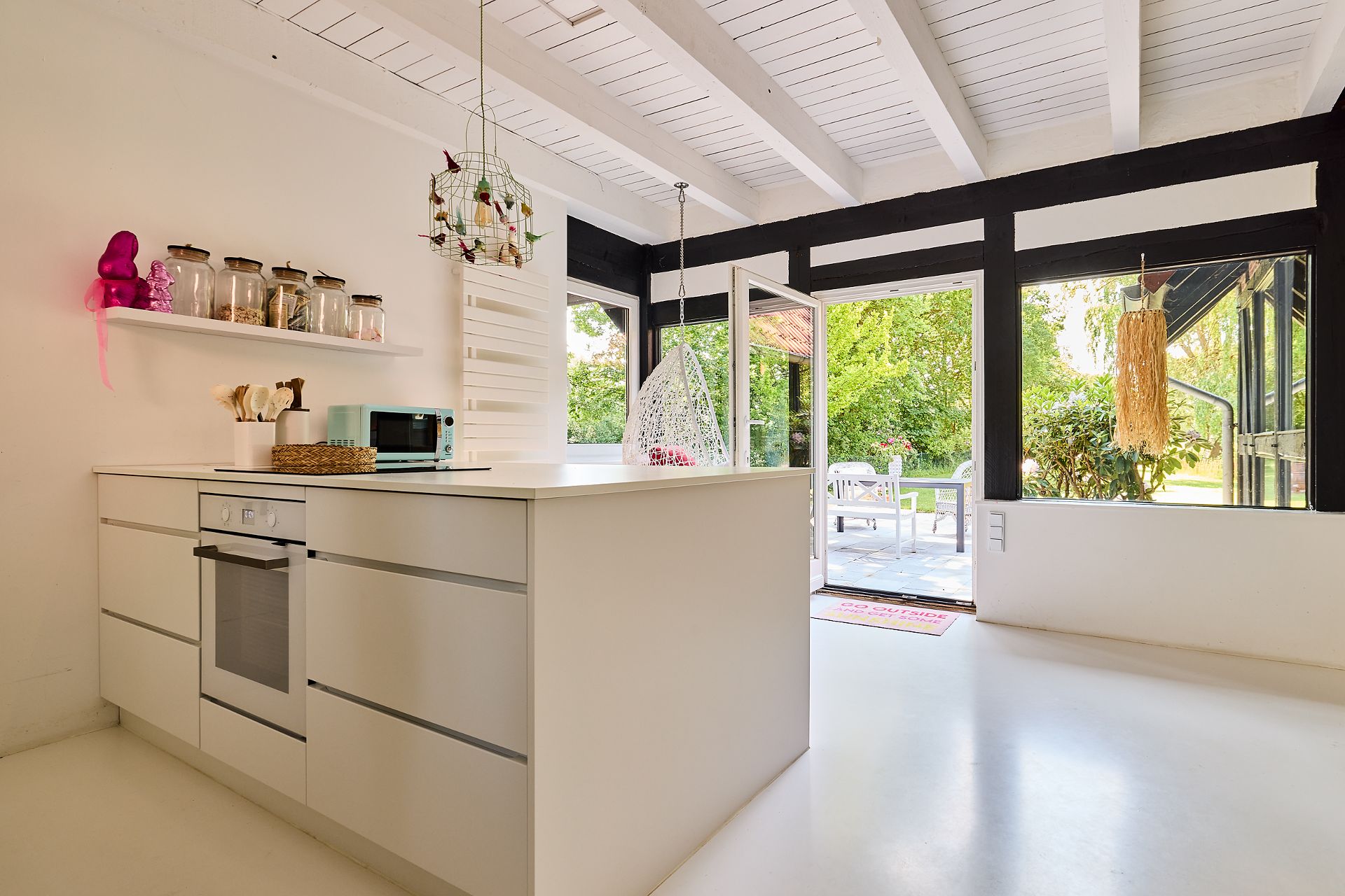 Helle, moderne Küche mit weißer Insel, Hängesessel und Blick auf Terrasse und Garten.