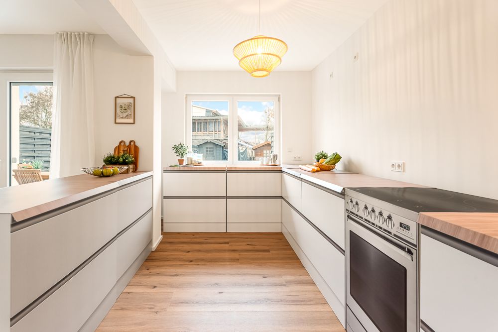 Helle, moderne Küche mit Holzarbeitsplatten, Laminatboden und großem Fenster.