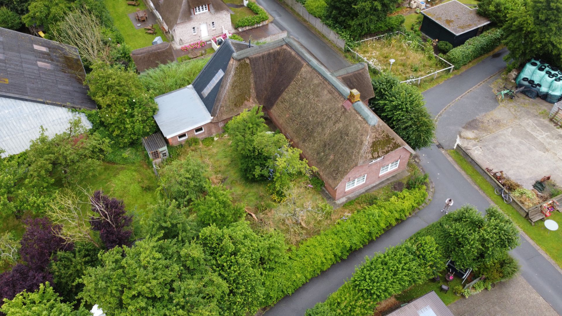 Luftaufnahme eines Hauses mit Reetdach, umgeben von Grünflächen und kleinen Straßen.