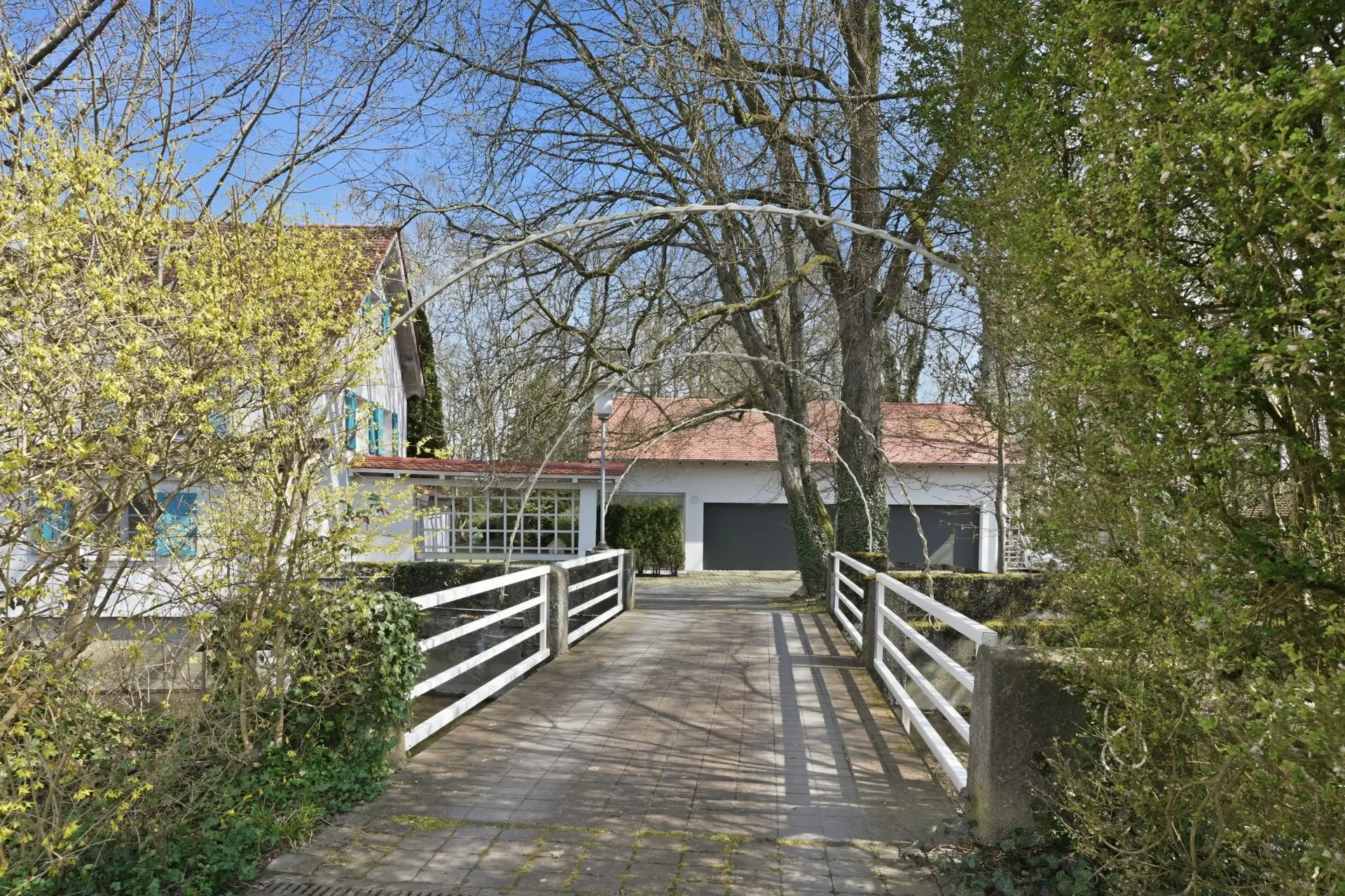 Weg mit Geländer führt zu einem Wohnhaus mit zwei Garagentoren, umgeben von Bäumen.
