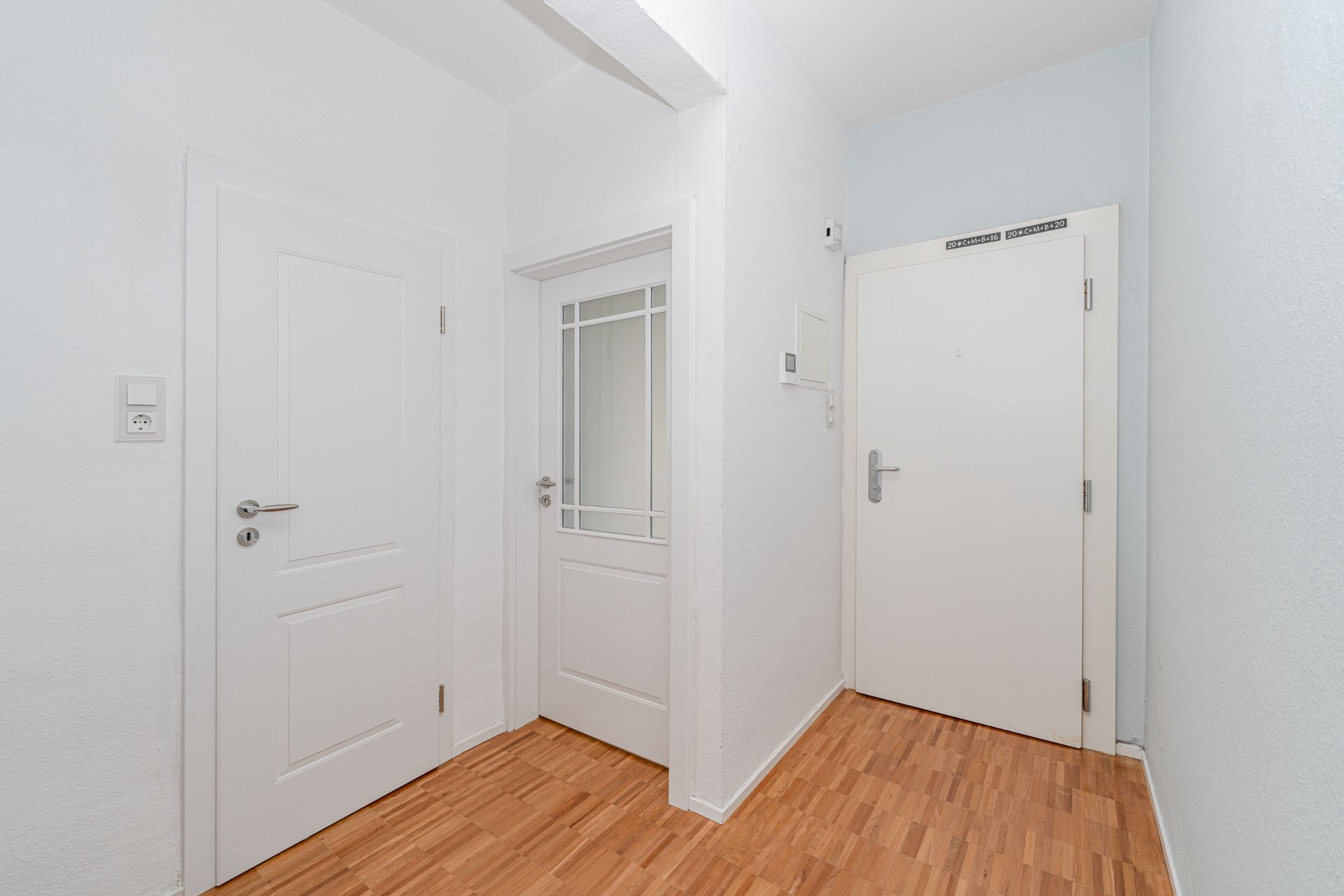 Heller Flur mit drei weißen Türen und Parkettboden in einer Wohnung.