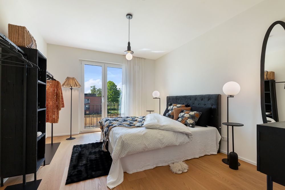 Modernes Schlafzimmer mit Doppelbett, Kleiderständer, Nachttischen und großem Fenster mit Blick nach draußen.