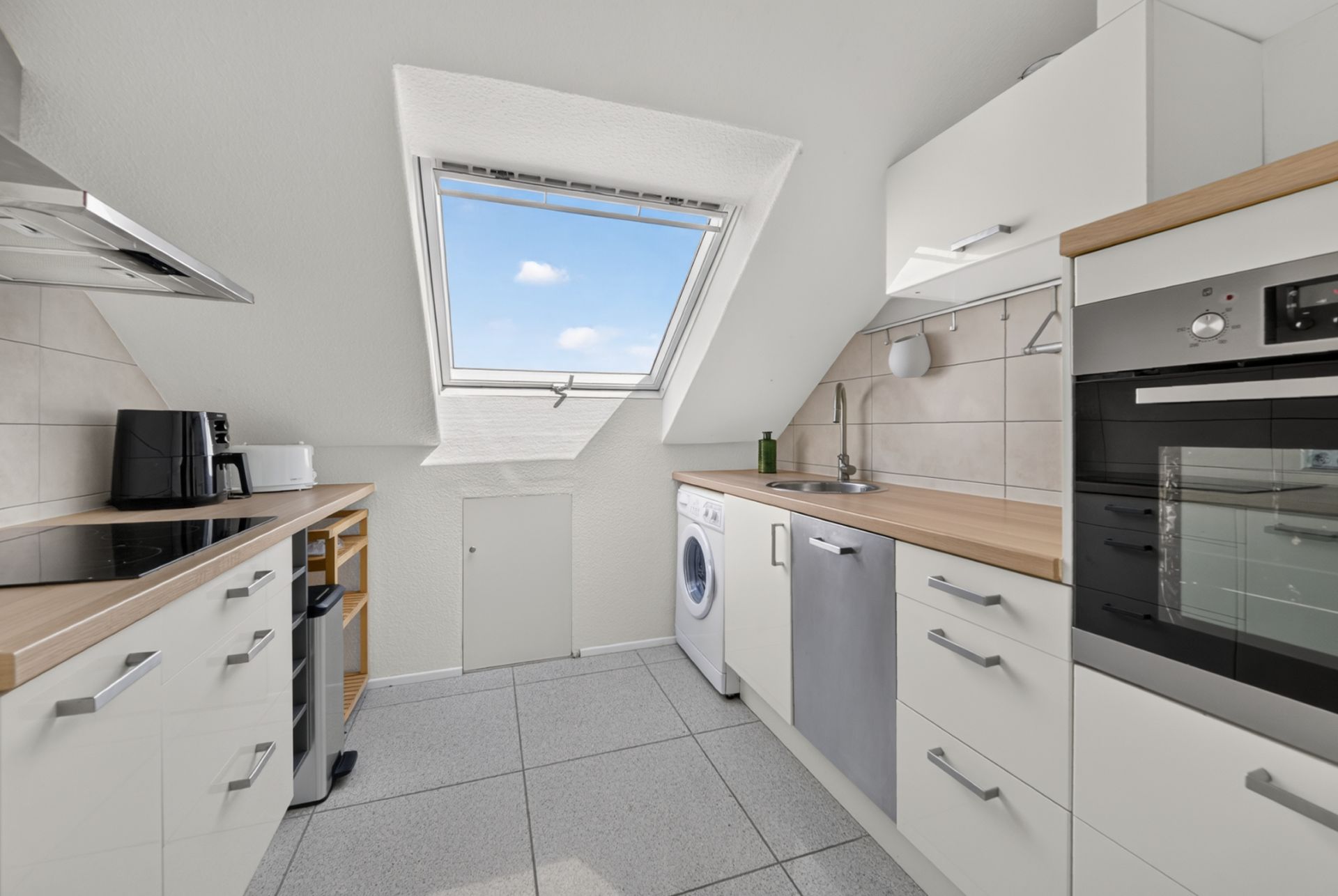 Moderne Küche mit Dachfenster, Herd, Backofen, Spüle und Waschmaschine.