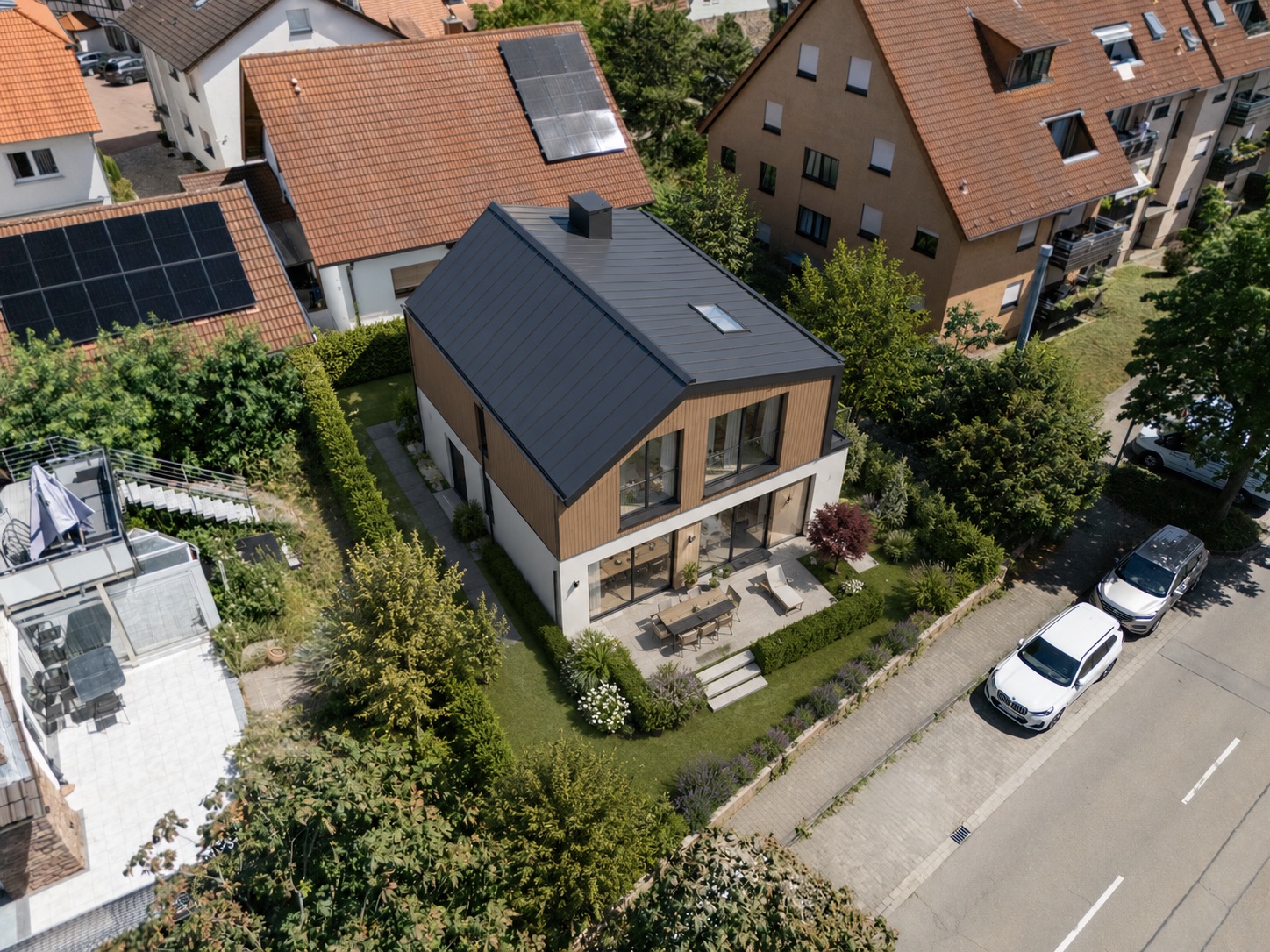 Luftaufnahme eines modernen Einfamilienhauses mit Garten und Terrasse in einer Wohnsiedlung.